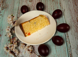 Easter composition. Eggs, a branch of a blooming apricot and a piece of glazed Easter cake close-up on a white plate on a light wooden background. Happy Easter Holidays. Selective focus.
