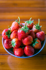 Fresh strawberries in a bowl on wooden table with low key scene