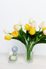 Easter eggs in a glass and yellow tulips in a vase on a light background