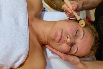 Masseuse giving a facial massage to a client with wood therapy
