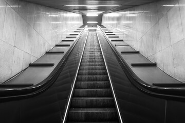 Perspective of mobile staircase in Milan's underground station. Light at the end of the tunnel. Monochromatic.