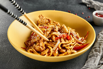 Hoisin chicken udon noodles. Yellow plate with wooden chopstick on dark slate table. Asian, authentic food concept