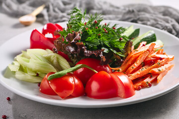 Raw Food - Fresh Vegetable Plate. White plate with healthy organic food on grey table. Tomato, Celery, Cucumber and Radish Vegetable and Fresh Greens. Produce, Healthy, Vegetarian rustic food concept.