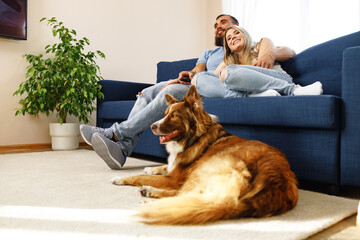 Young loving couple relaxing in living room with their dog pet