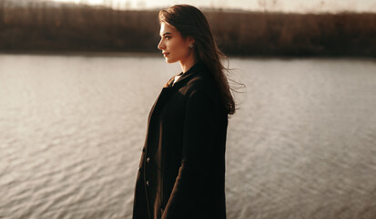 Thoughtful woman standing near lake in autumn day