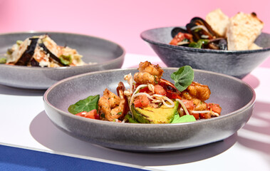 Shrimp and Avocado Grill restaurant plate. Restaurant appetizer food plate on white table with pink wall. Day sunlight with hard shadow of monstera palm leaves. Summer, spring restaurant food concept.