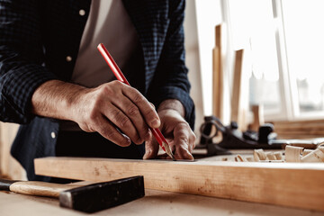Carpenter makes pencil marks on a wood plank