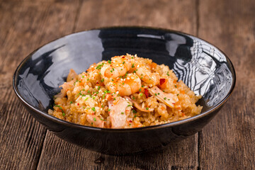 Asian seafood fried rice in a black bowl on the wooden table