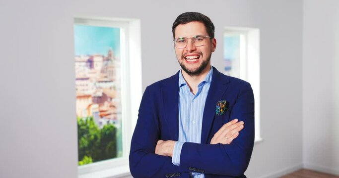 Camera approaching young tall happy Caucasian man real estate agency manager standing in empty house crossing His Arms, Smiling and looking at camera. Realtor concept. Selling property business.