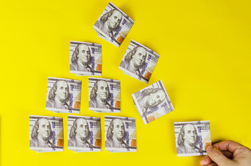 A hand pulls out a dollar banknote from the money pyramid on a yellow background.