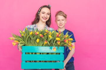 Family portrait sister and teenager brother with tulips on pink background