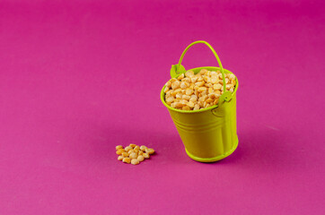 Fototapeta na wymiar Dry yellow peas and green bucket on a pink background.