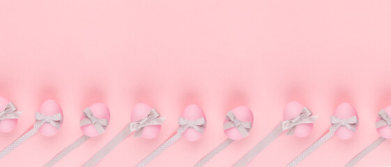 Elegant easter banner - pink eggs with silver bows and ribbon in row on pastel pink background.