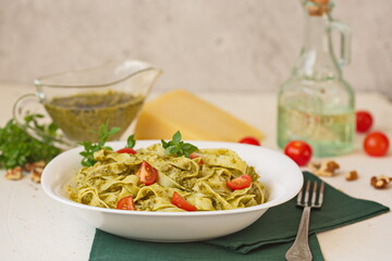 Fettuccine pasta with pesto sauce, pine nuts and parmesan on white plate. Decorated with cherry tomatoes. Italian cuisine. Restaurant, cafe, menu.