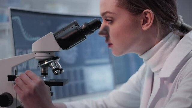 Female doctor working in laboratory. Studying medical samples. Looking through glassware and monitor