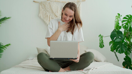 Young woman sitting on the bed with laptop celebrating a victory or success