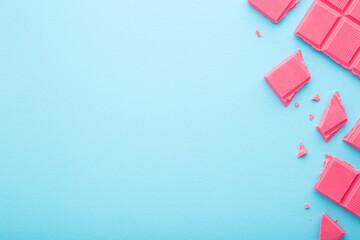 Broken pink chocolate pieces on light blue table background. Pastel color. Sweet snack. Closeup. Empty place for text. Top down view.