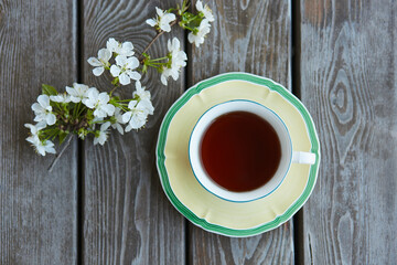 A cup of tea on a wooden background with a cherry branch