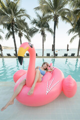 Woman sitting on pink inflatable mattress flamingos in the pool near the beach.