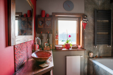 Interior of stylish bathroom in a cottage. Bathroom with wooden mirror and counter, bath, red sink...