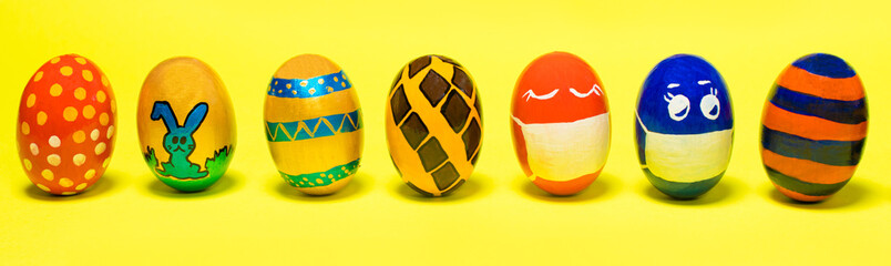 Multicolored Easter eggs on a yellow background. Eggs with faces put on protective masks against coronavirus during quarantine
