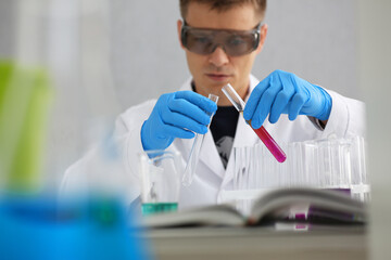 A male chemist holds test tube of glass in his hand overflows a liquid solution of potassium permanganate conducts an analysis reaction takes various versions of reagents using chemical manufacturing