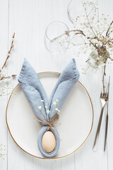 Table setting with egg in blue Easter Bunny napkin on golden rim plate. Top view.
