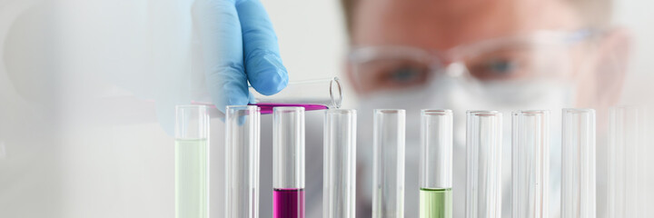 A male chemist holds test tube of glass in his hand overflows a liquid solution of potassium...