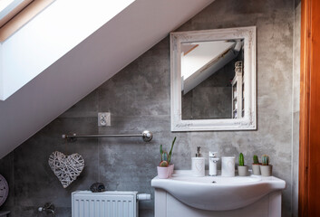 Bathroom sink with faucet and cactus and mirror on grey tiles in small bathroom in the attic with window. Hotel room.