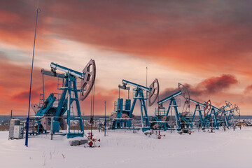 At the orange sunset dawn of the sky with clouds seven Oil pumpjack winter working. Oil rig energy...