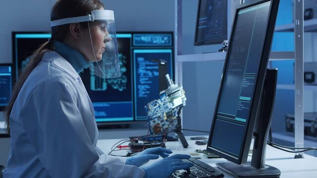 Female microelectronics engineer works in a modern scientific laboratory on computing systems and microprocessors. Electronic factory worker is testing the motherboard and coding the firmware.