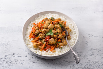 Vegan stew soy meat and vegetables served with boiled rice and greens on light gray textured...