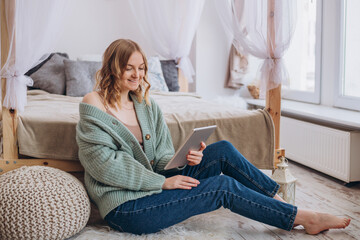 Obraz premium Young beautiful happy girl she buys goods online or works at home. Woman using tablet over room background, online communication or shopping concept