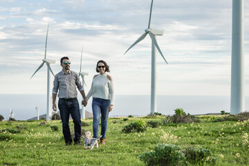 Happy couple walking with dog in field with windmills