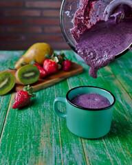 arándanos licuados y vertido en una taza de café, con una selección de fruta en una tabla de corte