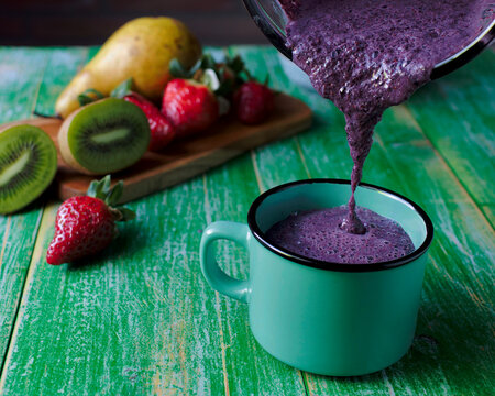 ar&aacute;ndanos licuados y vertido en una taza de caf&eacute;, con una selecci&oacute;n de fruta en una tabla de corte