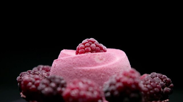 Berry mousse cake decorated with berries, rotating on black background. Close up