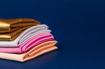 A stack of multi-colored satin fabric on a blue background, space for text