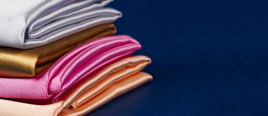 A stack of multi-colored satin fabric on a blue background, space for text