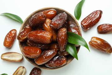 Bowl of dried dates with leaves on white background