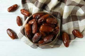 Bowl of dried dates on kitchen napkin on white wooden background