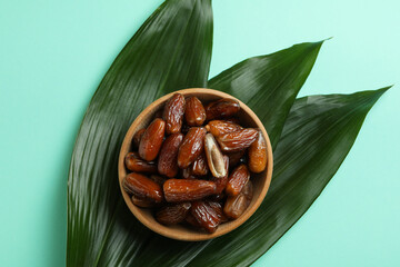 Bowl of dried dates and leaves on mint background