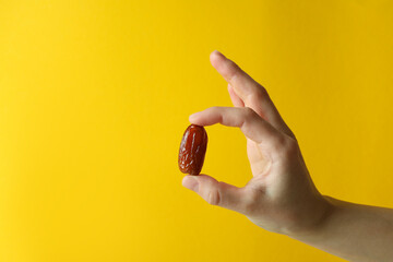 Female hand hold date fruit on yellow background