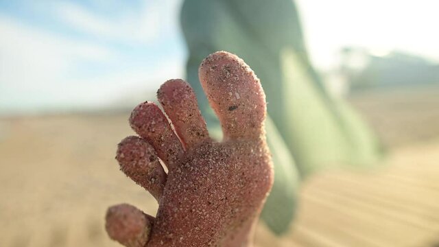 Close-up of foot and toes in the sand of a young girl in slow motion. Wiggles toes on a sandy beach on a sunny day