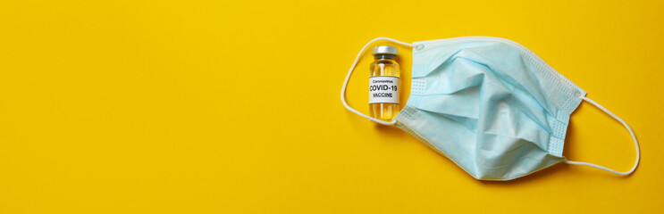 Vial of Covid - 19 vaccine and mask on yellow background