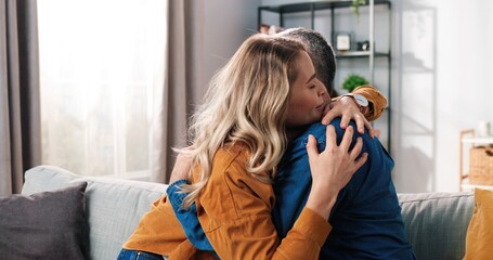 Side view of Caucasian middle-aged married couple wife and husband cheating having conversation and hugging reconciled after quarrel sitting on couch at home in cozy room, close up concept