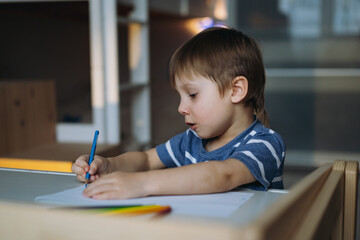 Adorable little toddler boy intensely drawing with color pencils. Image with selective focus