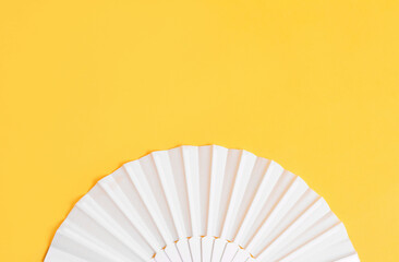 White hand fan on yellow background, top view. Space for text