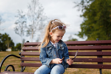 Little girl sitting on bench in spring park. Outdoors walk and child activity.