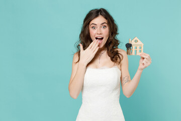 Shocked bride young woman 20s in white wedding dress hold house bunch of apartment keys cover mouth...